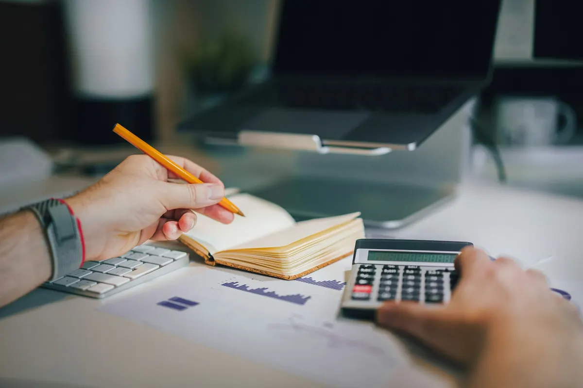 A person using a calculator and writing in a notebook on a desk