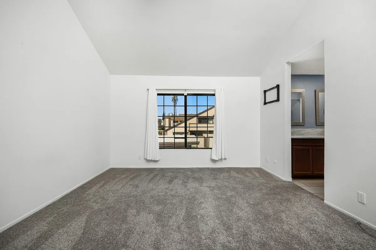 An empty room with a window and grey carpet