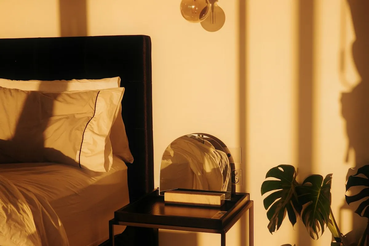 A warmly lit bedroom with a bed, a plant and a mirror