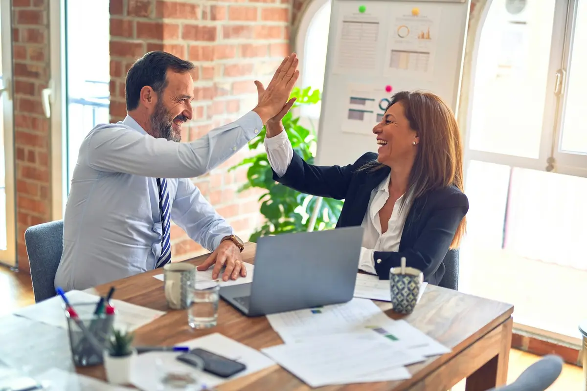 Two people at a desk giving each other a high five