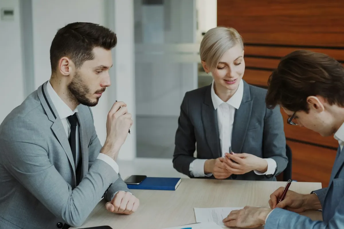 Three people at a table, one signing a contract