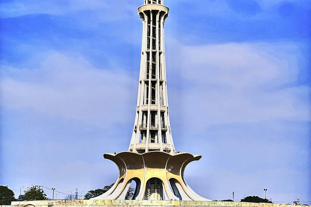 People walking along a street near a tall tower in Lahore