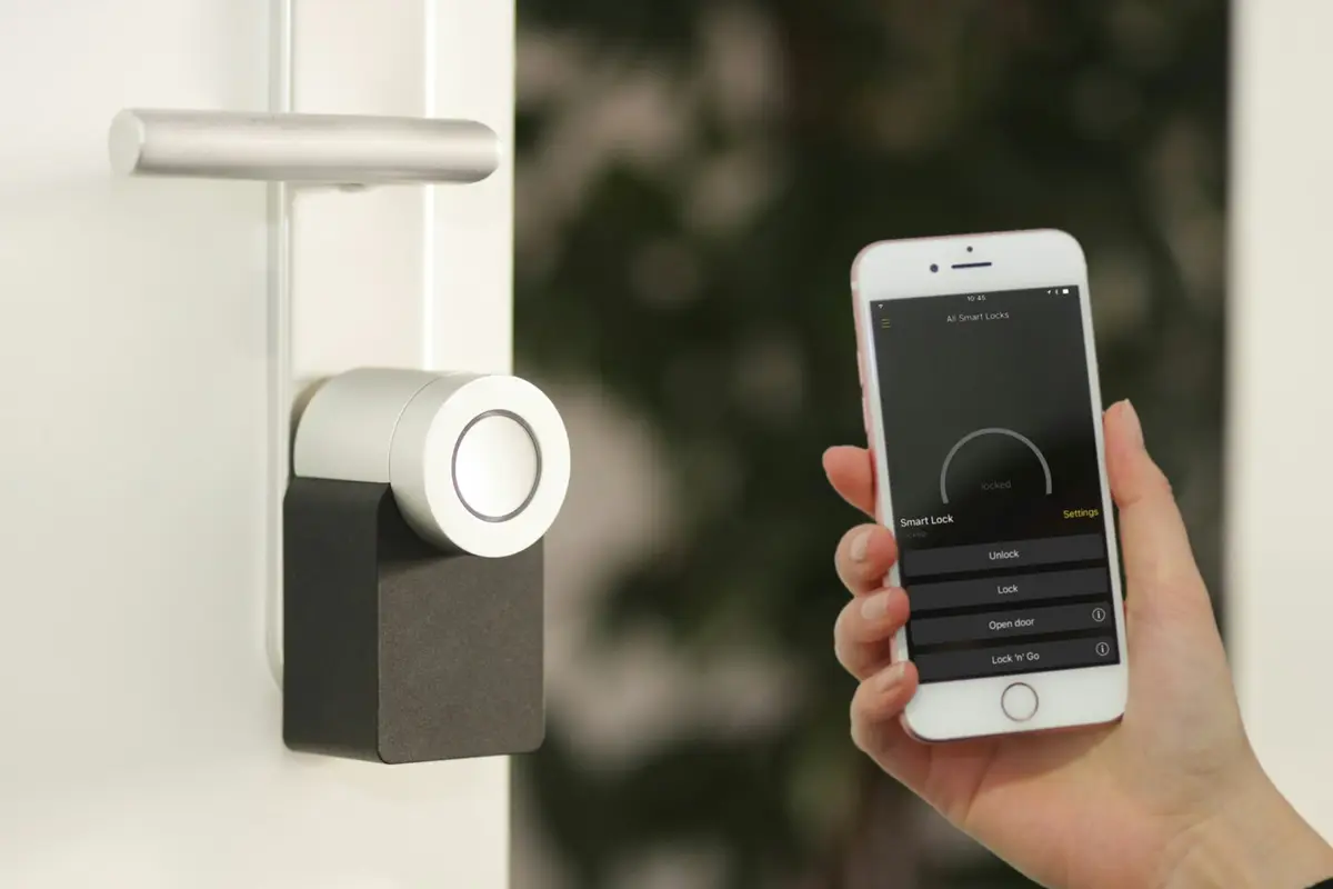 A hand holding a phone next to a smart door lock
