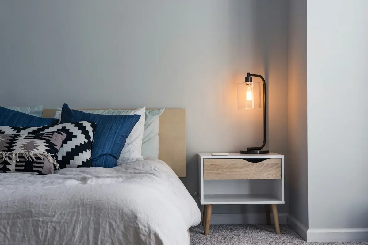 A simple bedroom with a made bed, a lamp and a bedside table