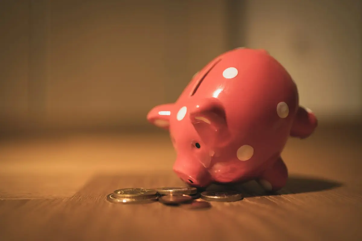 A pink piggy bank next to a few coins
